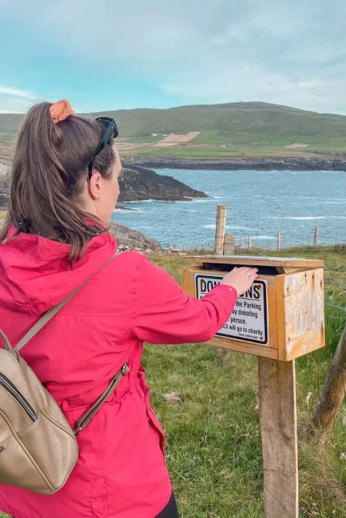 Woman donating to a parking box on a scenic Irish coast road