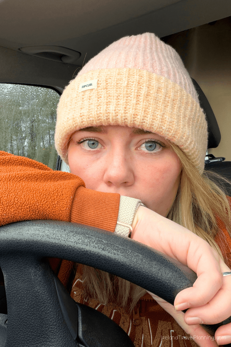 Woman in beanie and orange sweater in car, ready for Ireland travel.
