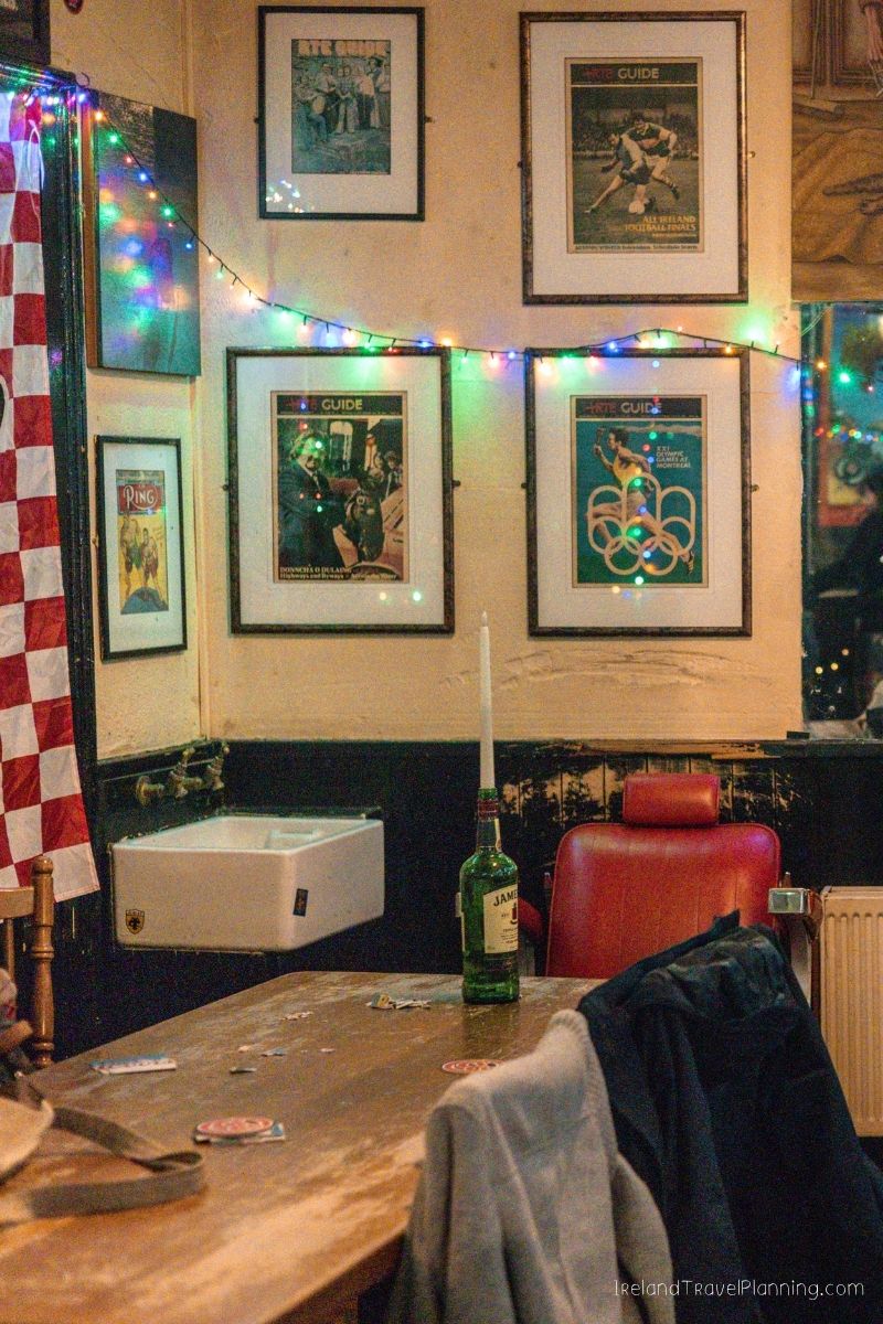 Cozy pub corner with framed posters, a sink, and a table with drinks.