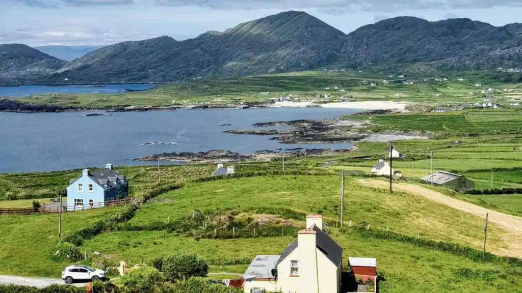 Coastal Ireland landscape with green hills and colorful houses.