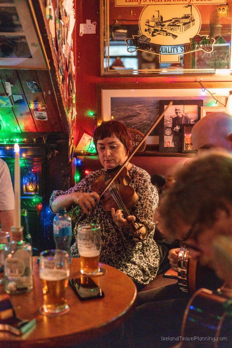 Woman plays violin in a cozy Irish pub with colorful lights