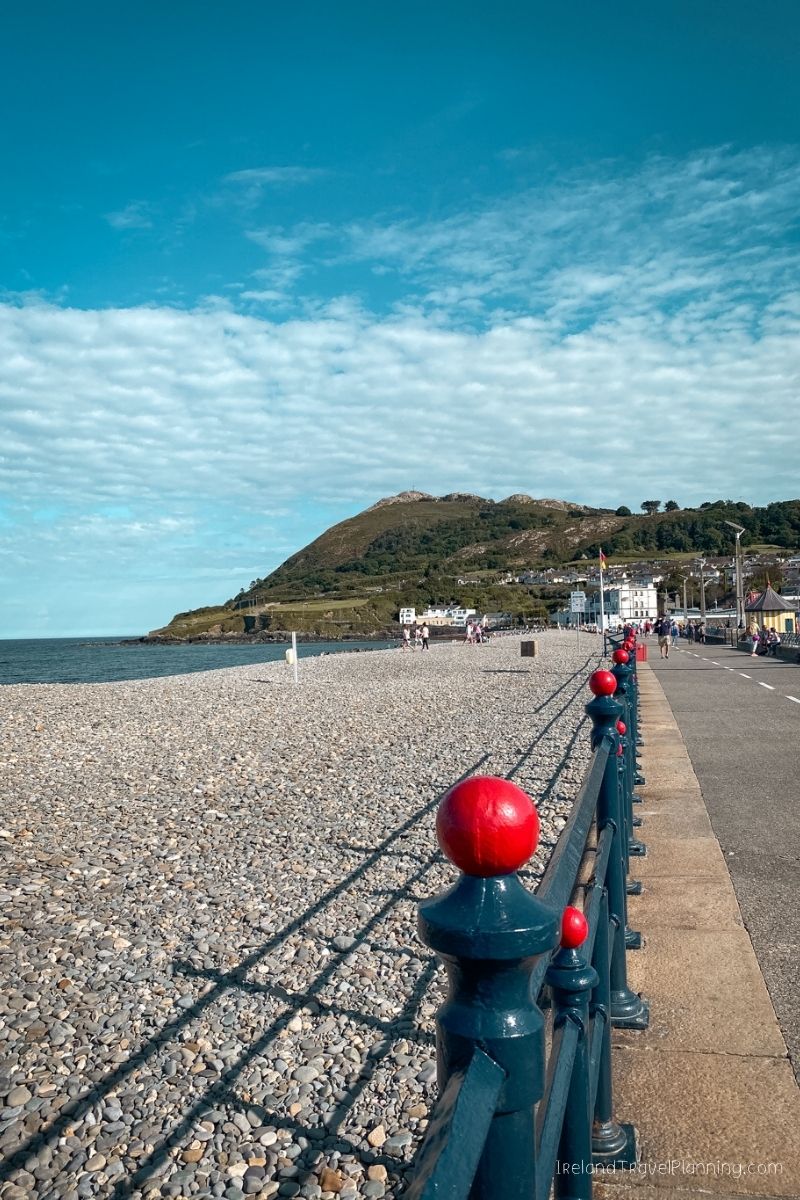 Pebble beach with a blue railing and red spheres, overlooking a hill with buildings. Free Dublin activity.