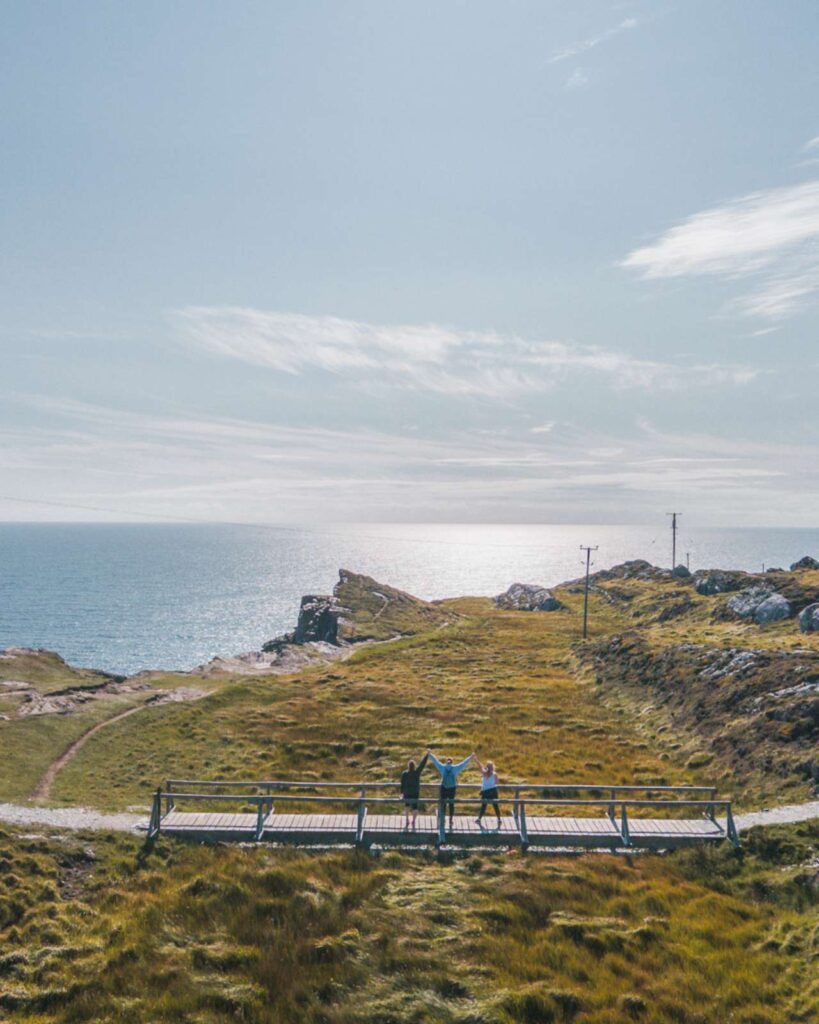 A drone shot of 3 friends on a boardwalk looking out at Ireland's Wild Atlantic Way on Sheeps Head in County Cork