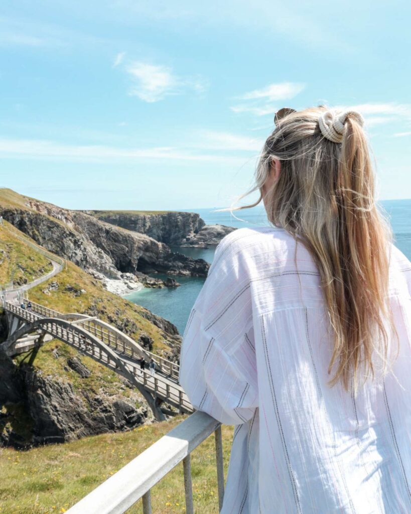 A woman standing with her back to the camera looking out at the coastal bridge at Mizen Head, County Cork, the South Western Tip of Ireland