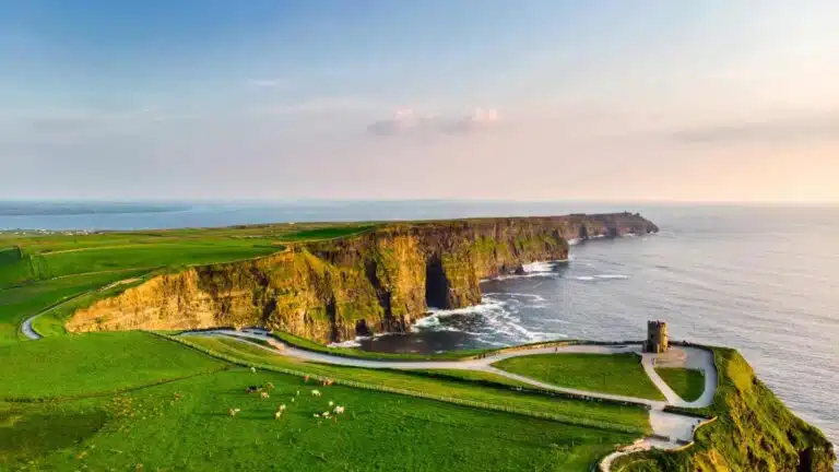 Scenic view of the Cliffs of Moher in Ireland with green fields and a historic tower.
