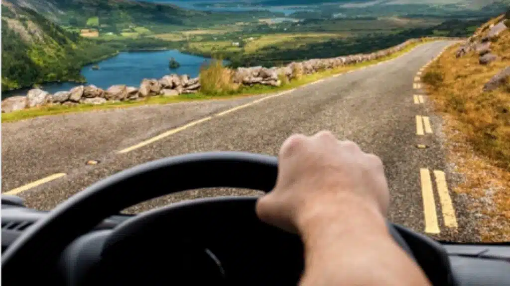 Driving in Ireland: View from car on winding road through scenic Irish countryside.