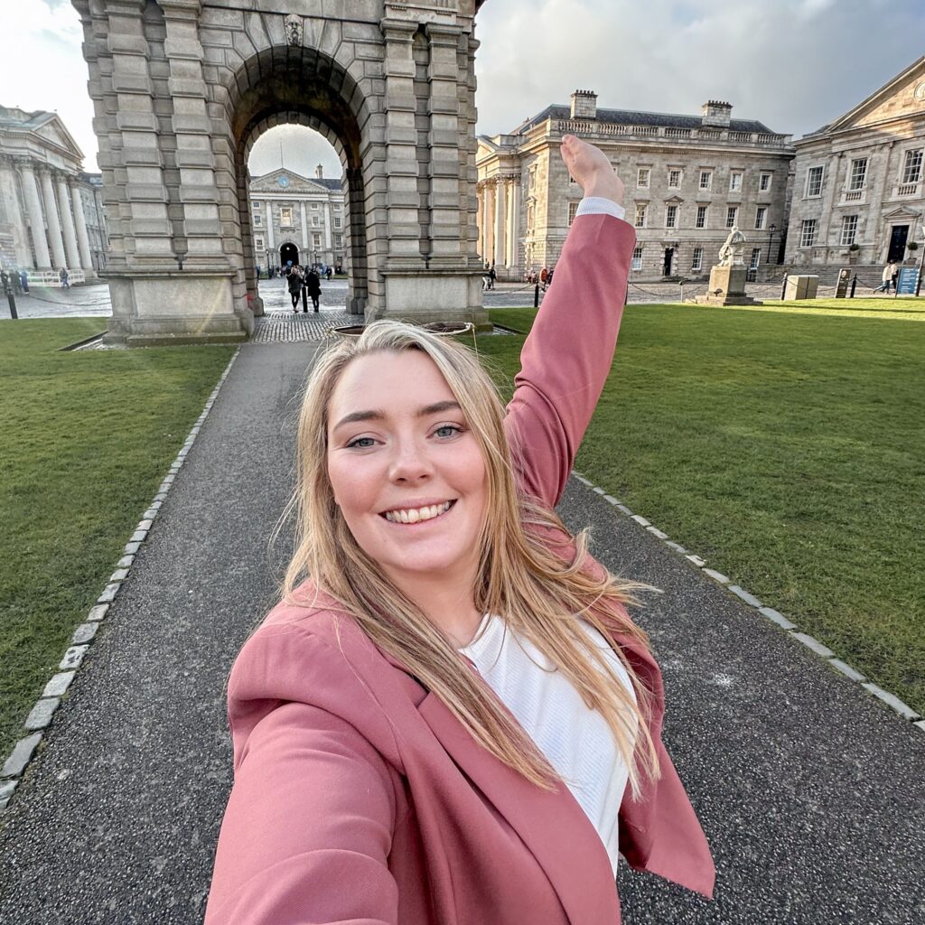 Woman in pink blazer at Trinity College Dublin, a popular spot for driving in Ireland.