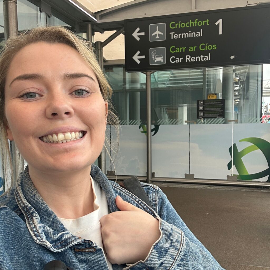 Woman at airport arrivals, Terminal 1, Car Rental sign, driving in Ireland