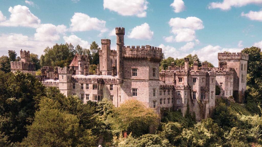 Lismore Castle, a famous Irish castle, surrounded by lush greenery under a partly cloudy sky.