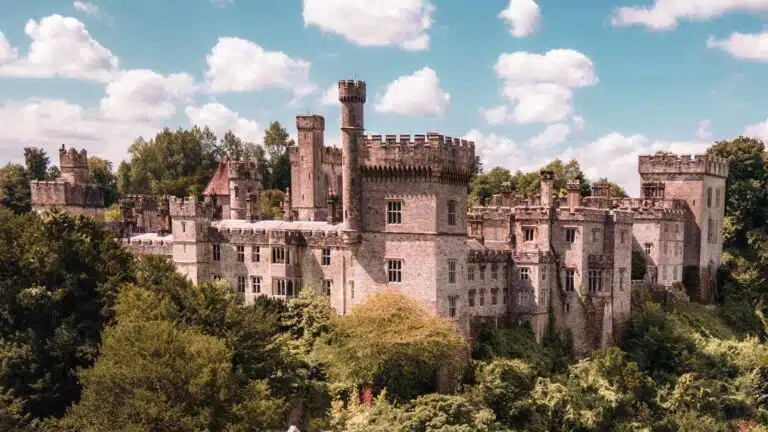Lismore Castle, a famous Irish castle, surrounded by lush greenery under a partly cloudy sky.