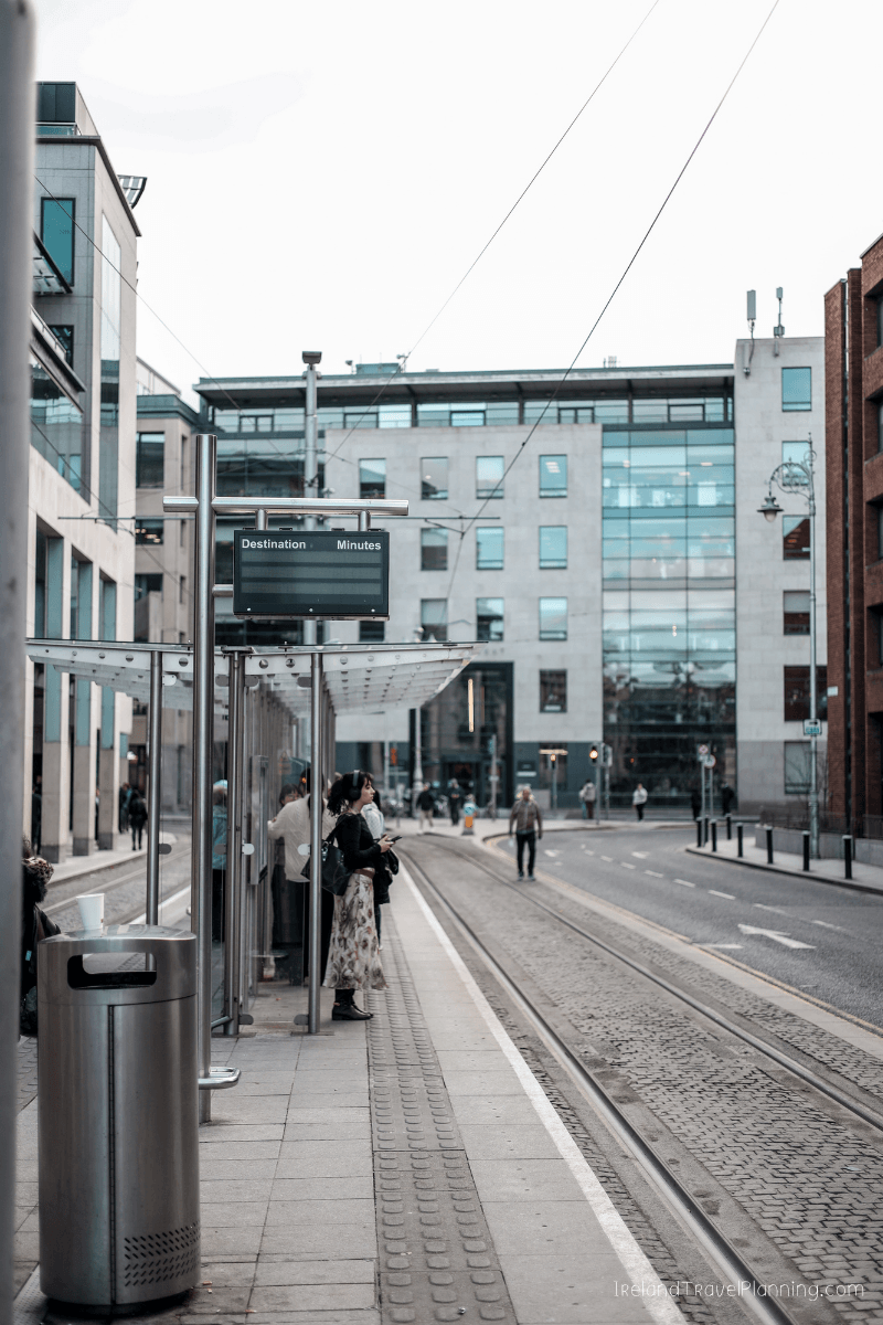 Dublin public transport: People waiting at a tram stop with a destination board.