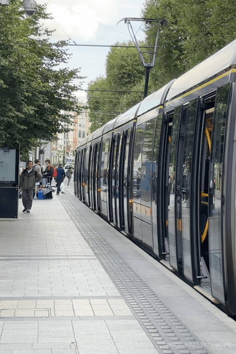 Dublin tram with open doors at a station, people waiting to board public transport.