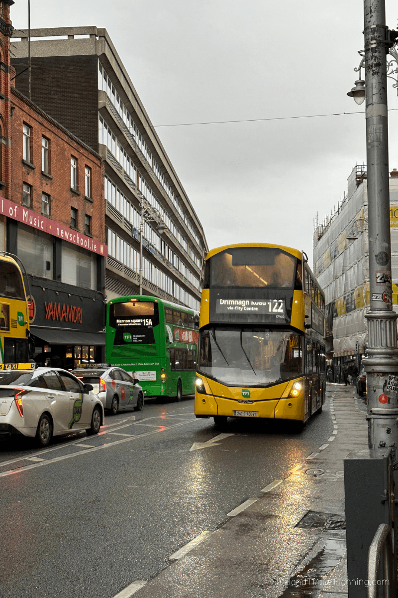 Yellow Dublin Bus 122 and green 15A on a wet city street, public transport in Dublin