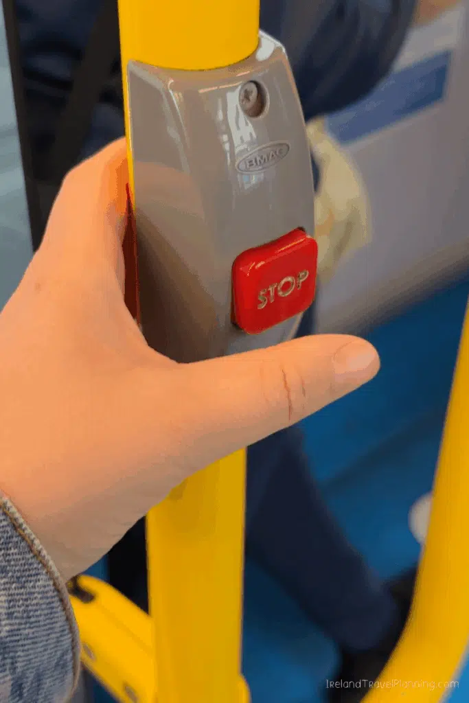 Close-up of a hand pressing a red "STOP" button on a yellow pole on Dublin public transport.