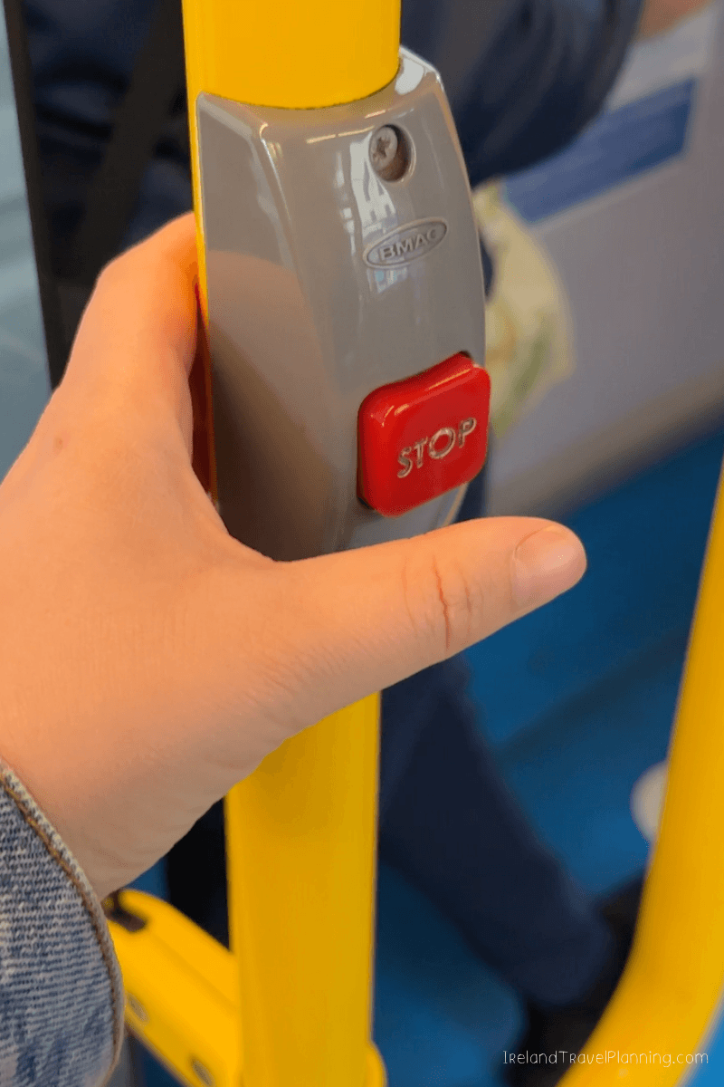Close-up of a hand pressing a red "STOP" button on a yellow pole on Dublin public transport.