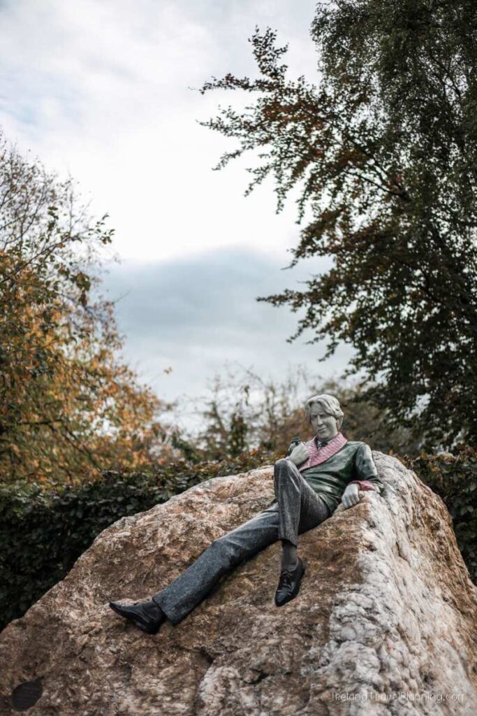 Oscar Wilde statue reclining on rock in Dublin park, a hidden gem.