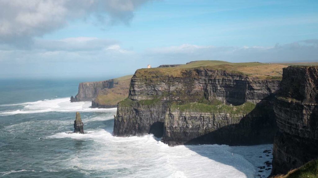 Cliffs of Moher, Ireland, with a sea stack and crashing waves under a blue sky