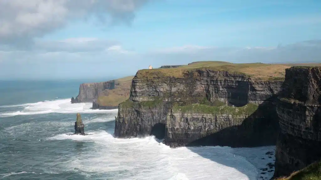 Cliffs of Moher, Ireland, with a sea stack and crashing waves under a blue sky