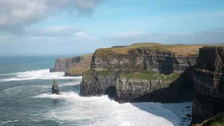 Cliffs of Moher, Ireland, with a sea stack and crashing waves under a blue sky