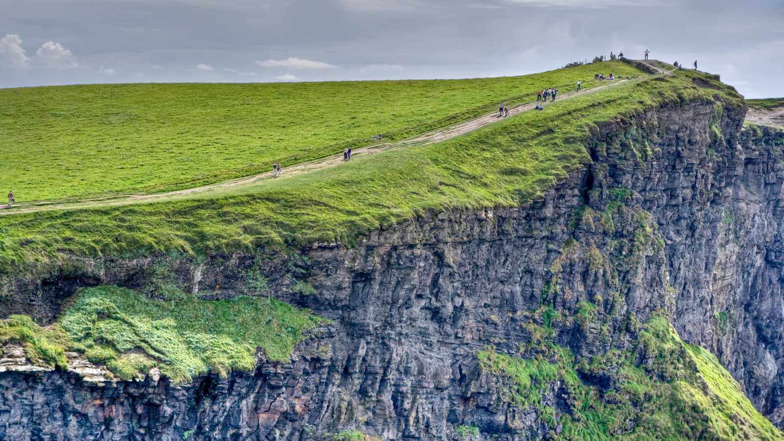 Tourists walking along the grassy edge of a tall cliff