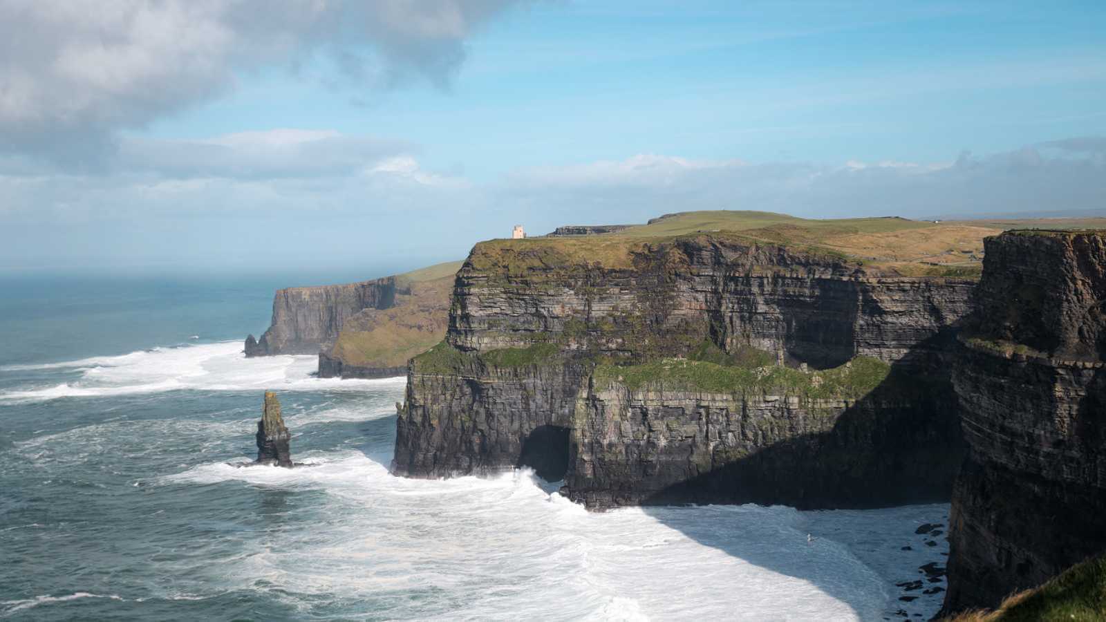 Rugged cliffs with grassy tops overlooking the ocean under a partly cloudy sky