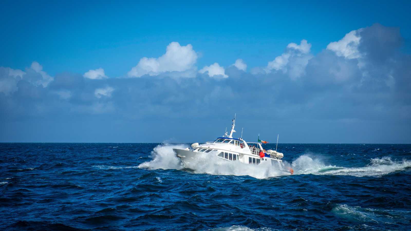 White passenger ferry cutting through the blue ocean under a partly cloudy sky.