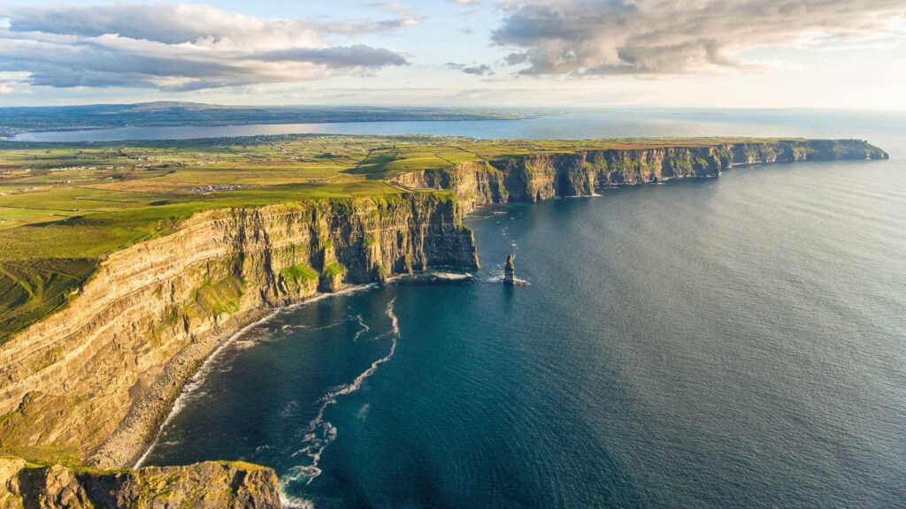 Cliffs of Moher, Ireland, with dramatic coastline and green fields under a cloudy sky.