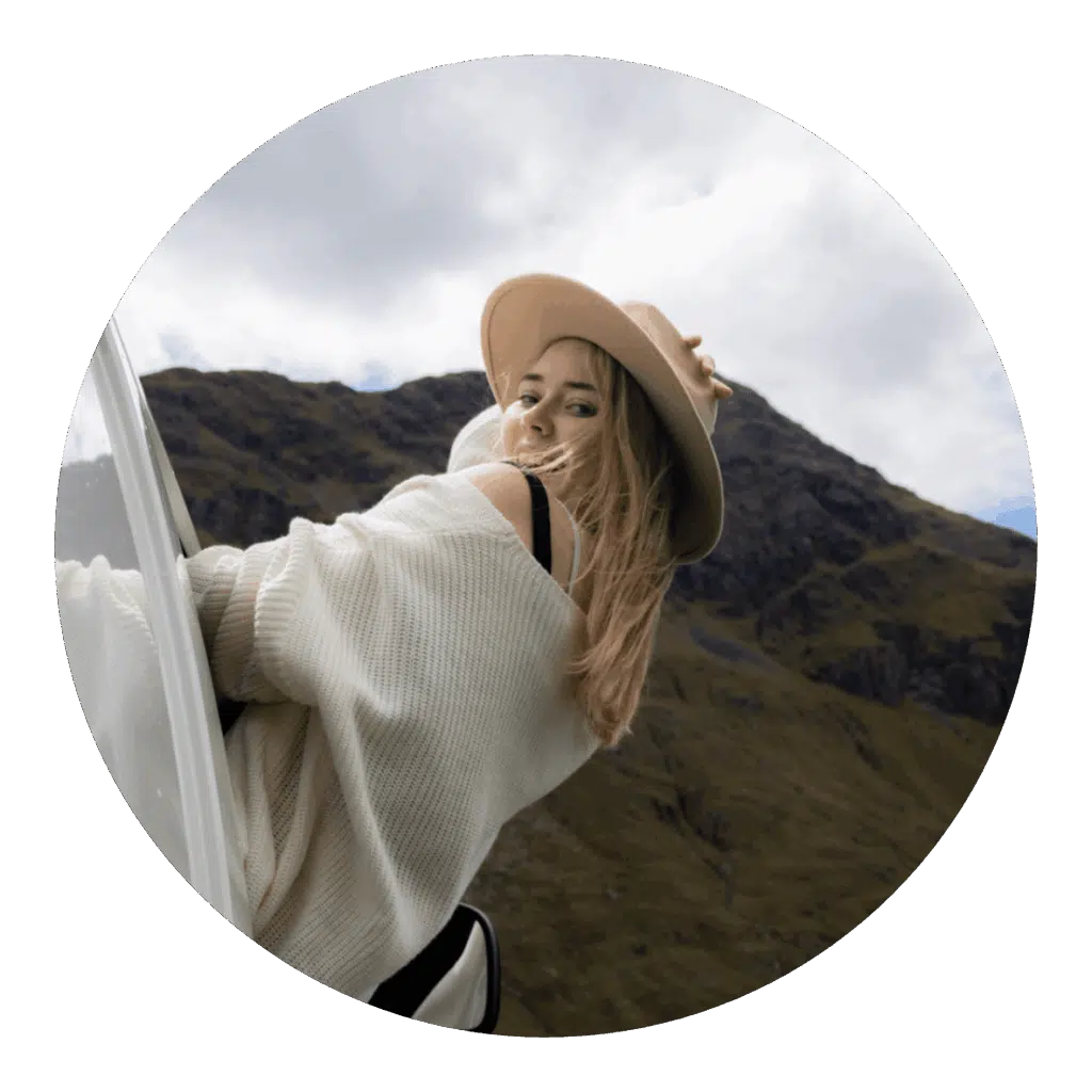 Woman in hat looks back from car window, mountain backdrop