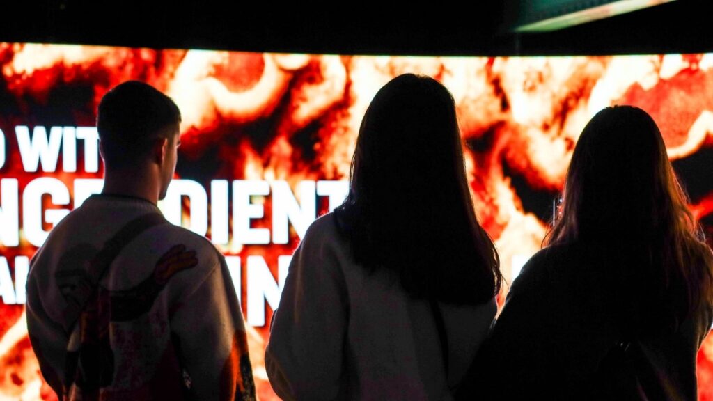 People looking at a large screen displaying text and an abstract image.