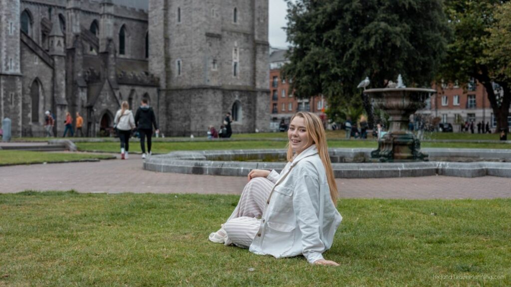 Woman sitting on the grass in Dublin near Christ Church Cathedral and a fountain.