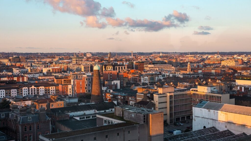 Dublin cityscape at sunset, featuring a brick tower and buildings under a pastel sky.