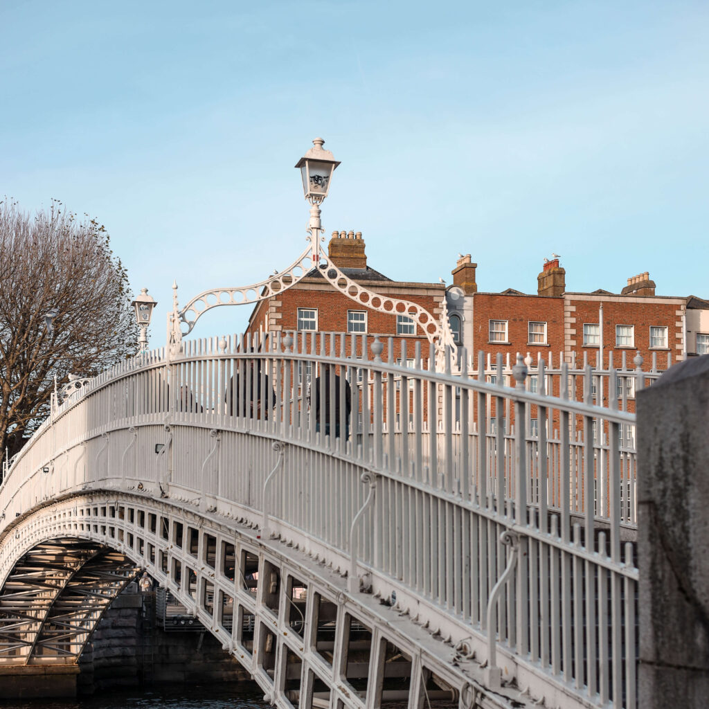 Dublin's Ha'penny Bridge, a white pedestrian bridge with ornate lamps, against a backdrop of red brick buildings.