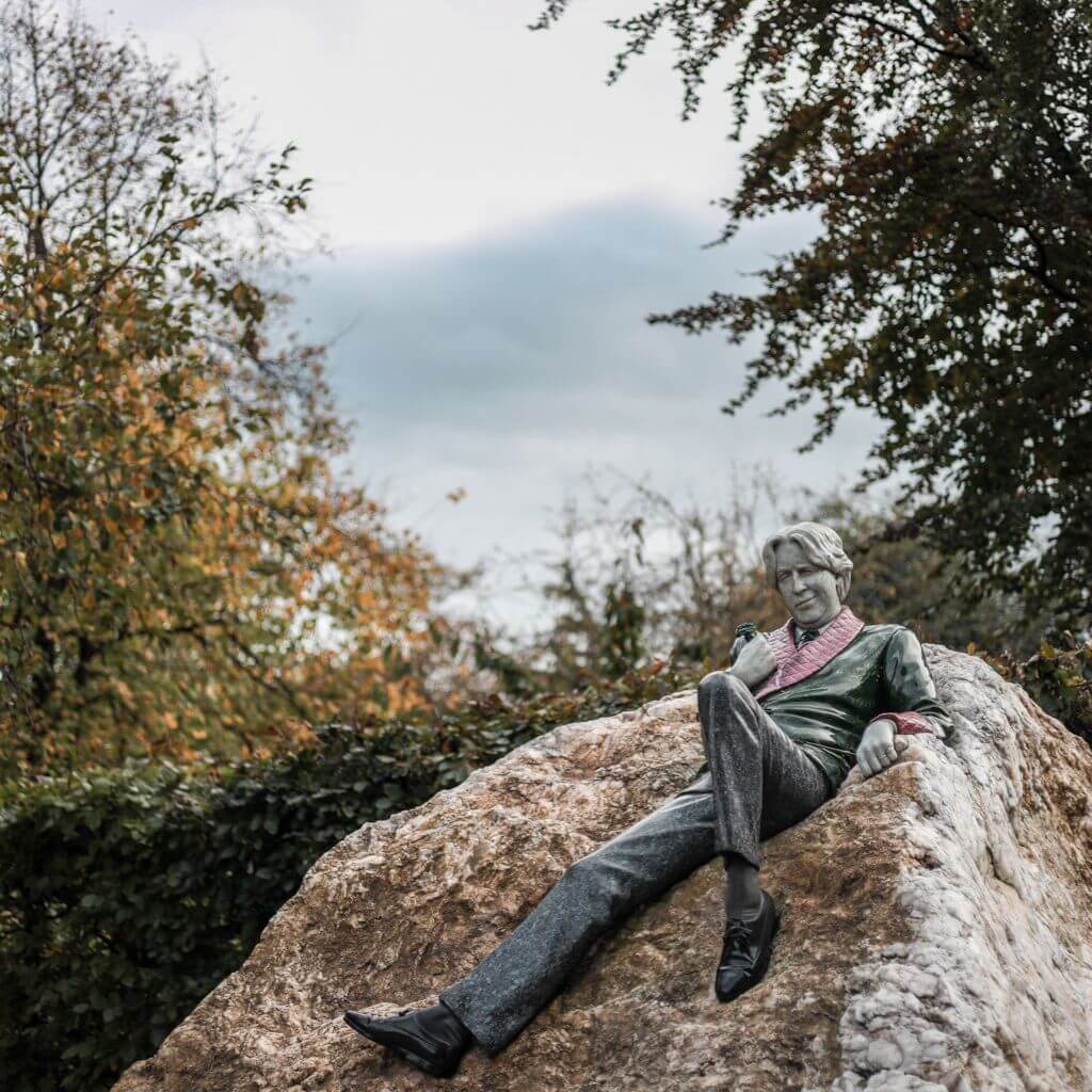 Oscar Wilde statue reclining on a rock in Dublin park.