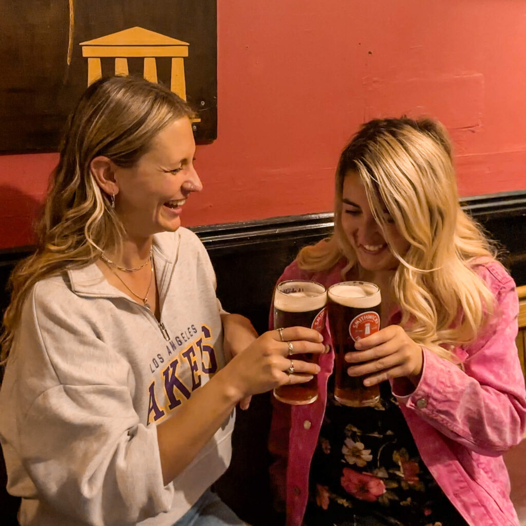 Two women toasting with pints of beer in a Dublin pub. Enjoying Dublin attractions.