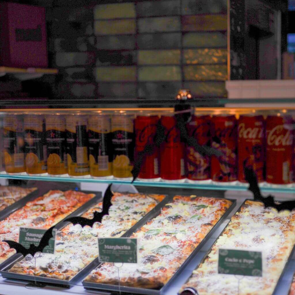Dublin pizza shop display: Margherita, Cacio e Pepe, Sausage. Drinks behind. Halloween bats on display.