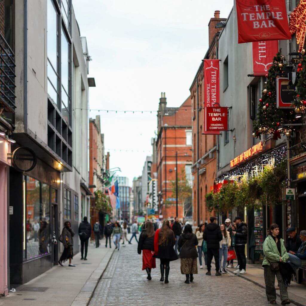Temple Bar street scene in Dublin, featuring pedestrians and traditional Irish pubs with flags and festive decorations.