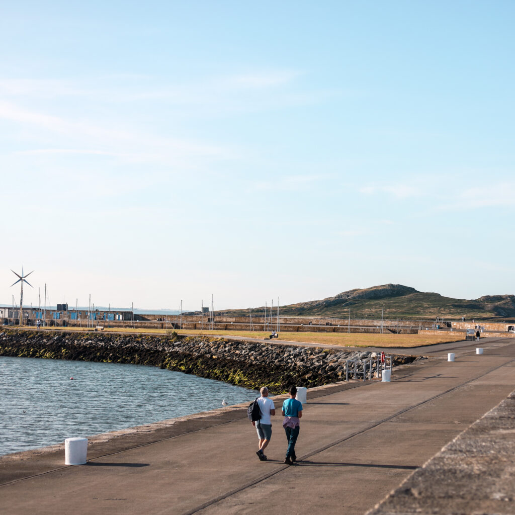 People walking on a pier in Dublin, with Howth Head in the distance.