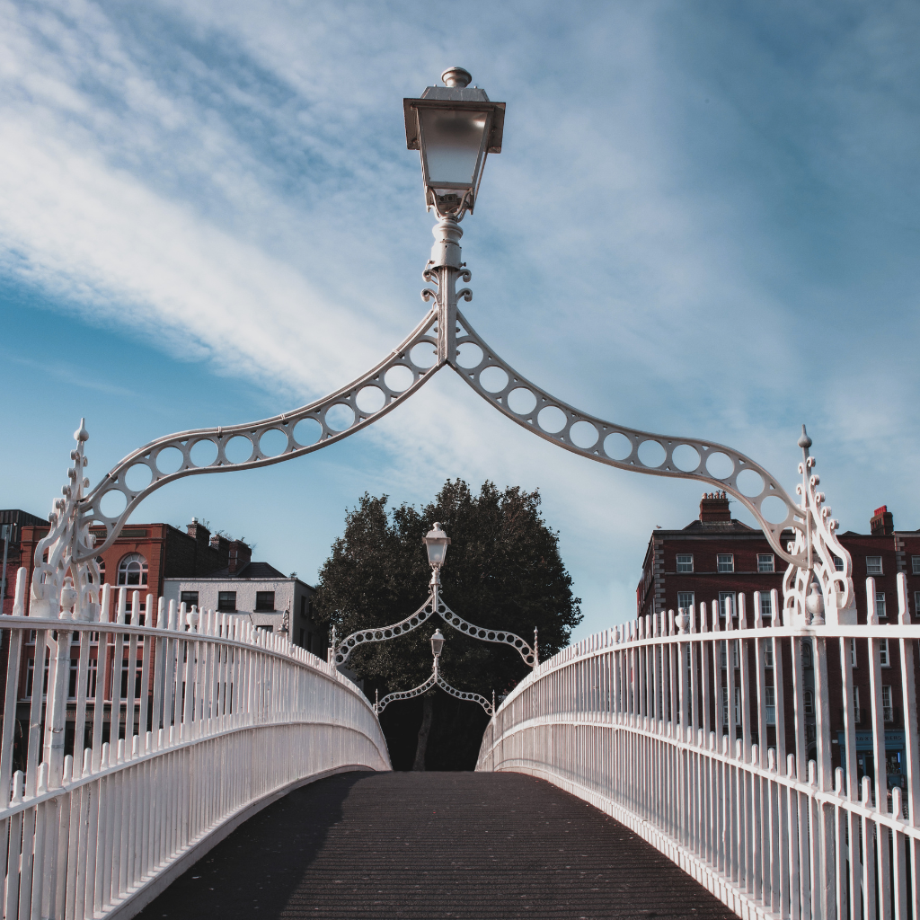 Dublin's Ha'penny Bridge: White pedestrian bridge with ornate lamp posts under a blue sky. Dublin attractions.
