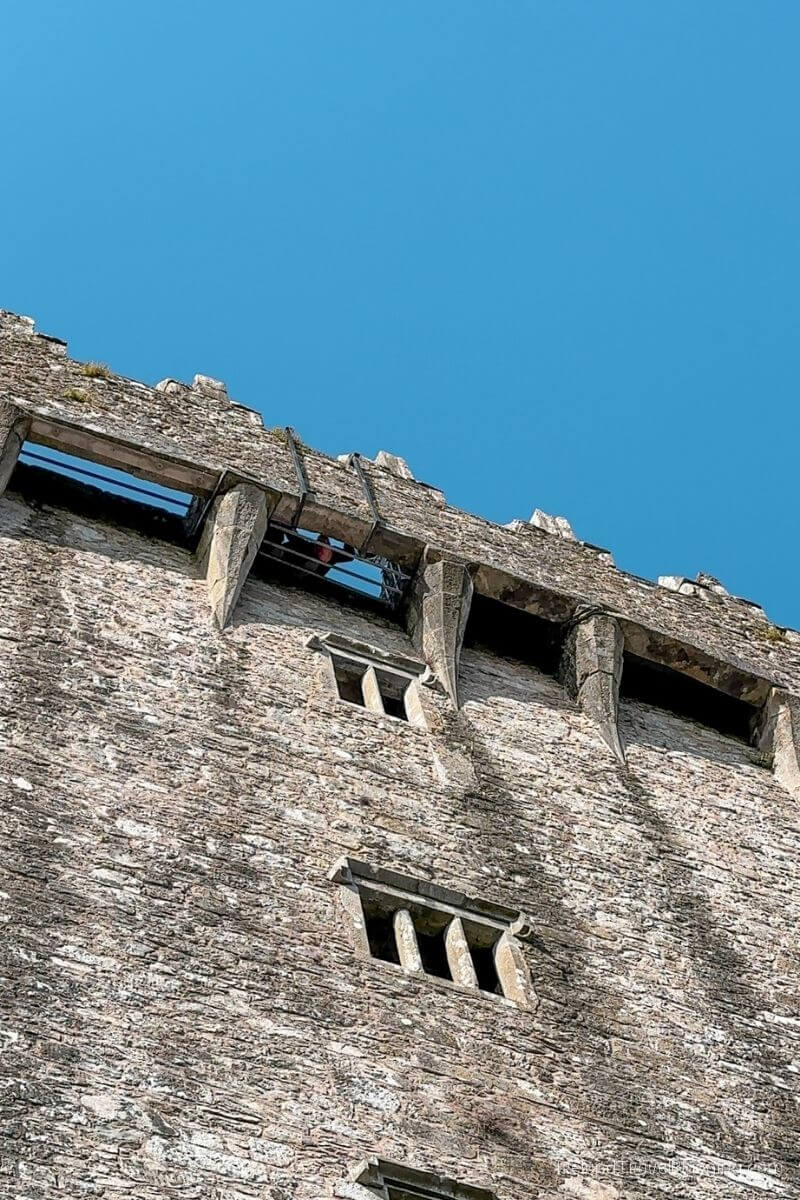 Stone castle wall with arrow slits and merlons under clear blue sky