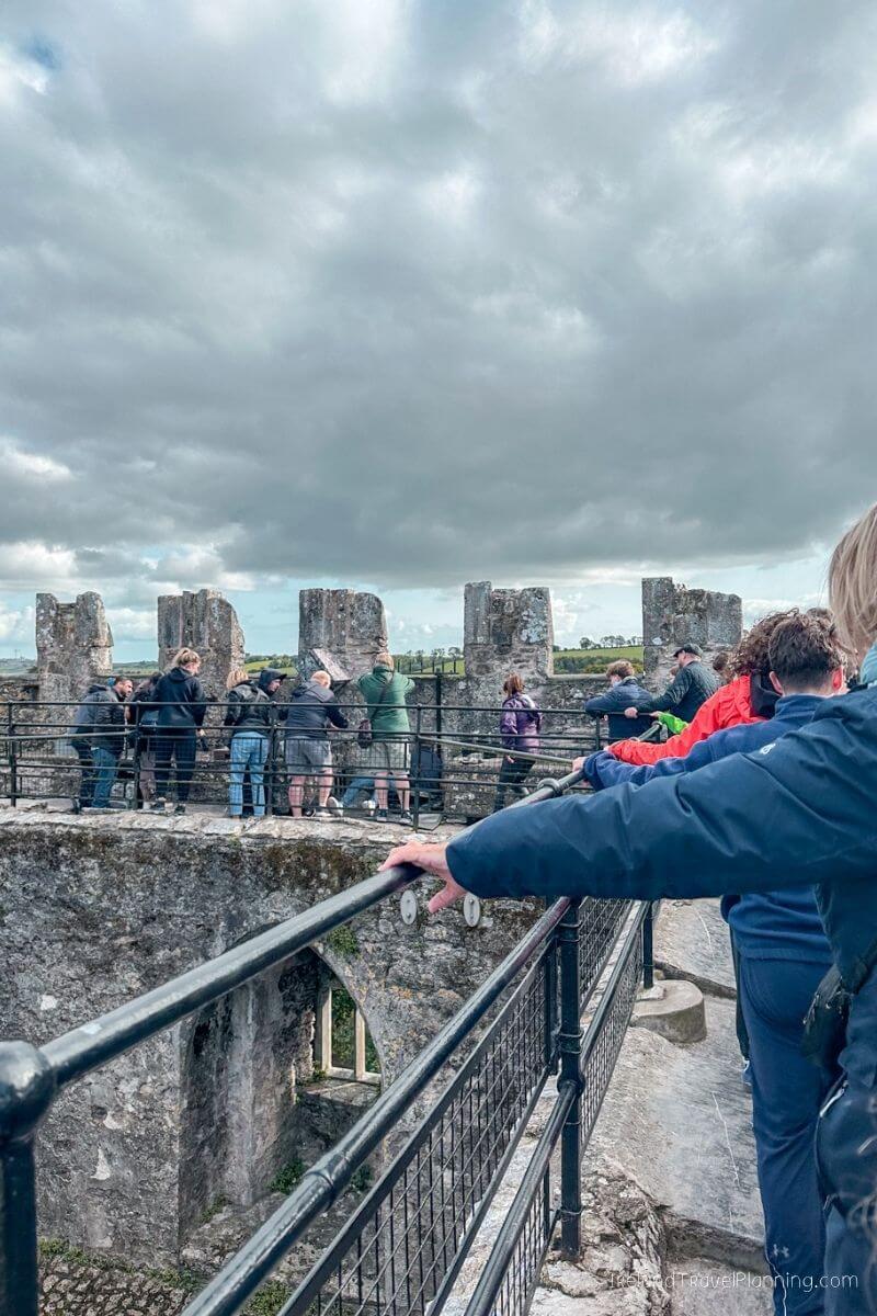 Tourists view Blarney Castle ruins under cloudy skies