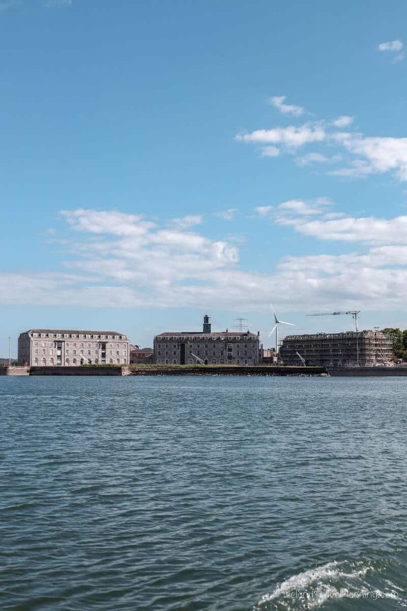 View of Cork City's waterfront with large buildings and a windmill under a partly cloudy sky