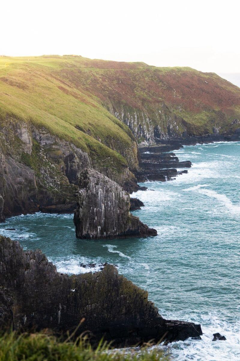 Dramatic cliffs and sea stacks on the coast of Cork, Ireland, with waves crashing.