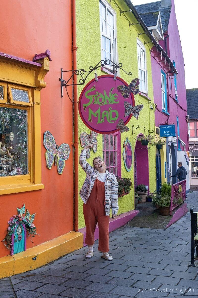 Woman in orange jumpsuit posing in front of vibrant Kinsale town store