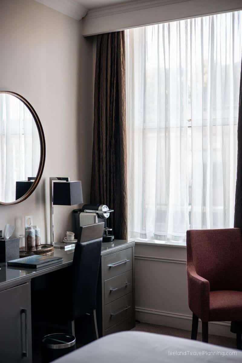 Hotel room desk with round mirror, chair, and window with white curtains