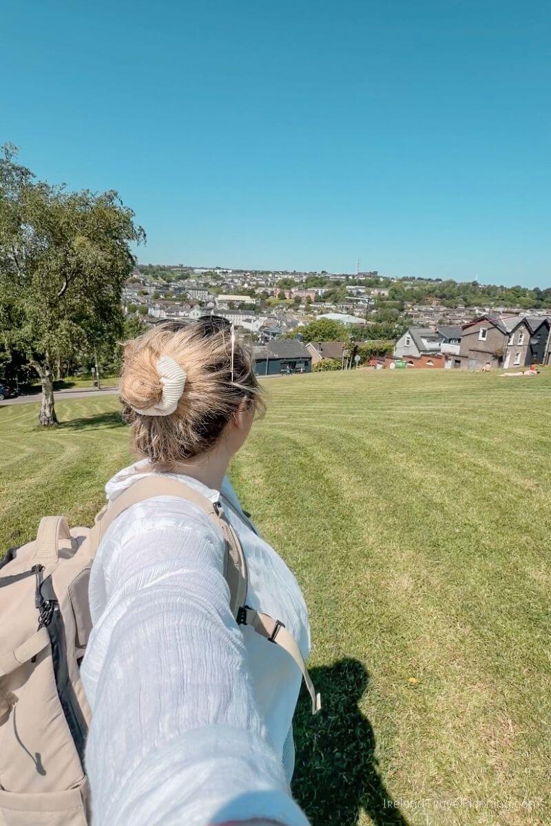 Woman with a backpack standing in a grassy field overlooking Cork City