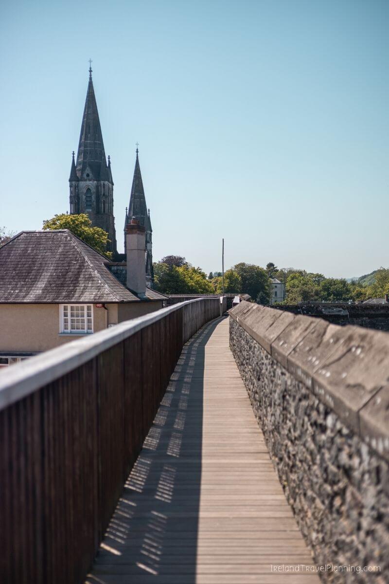 Wooden bridge over old stone wall with church spire in Cork City