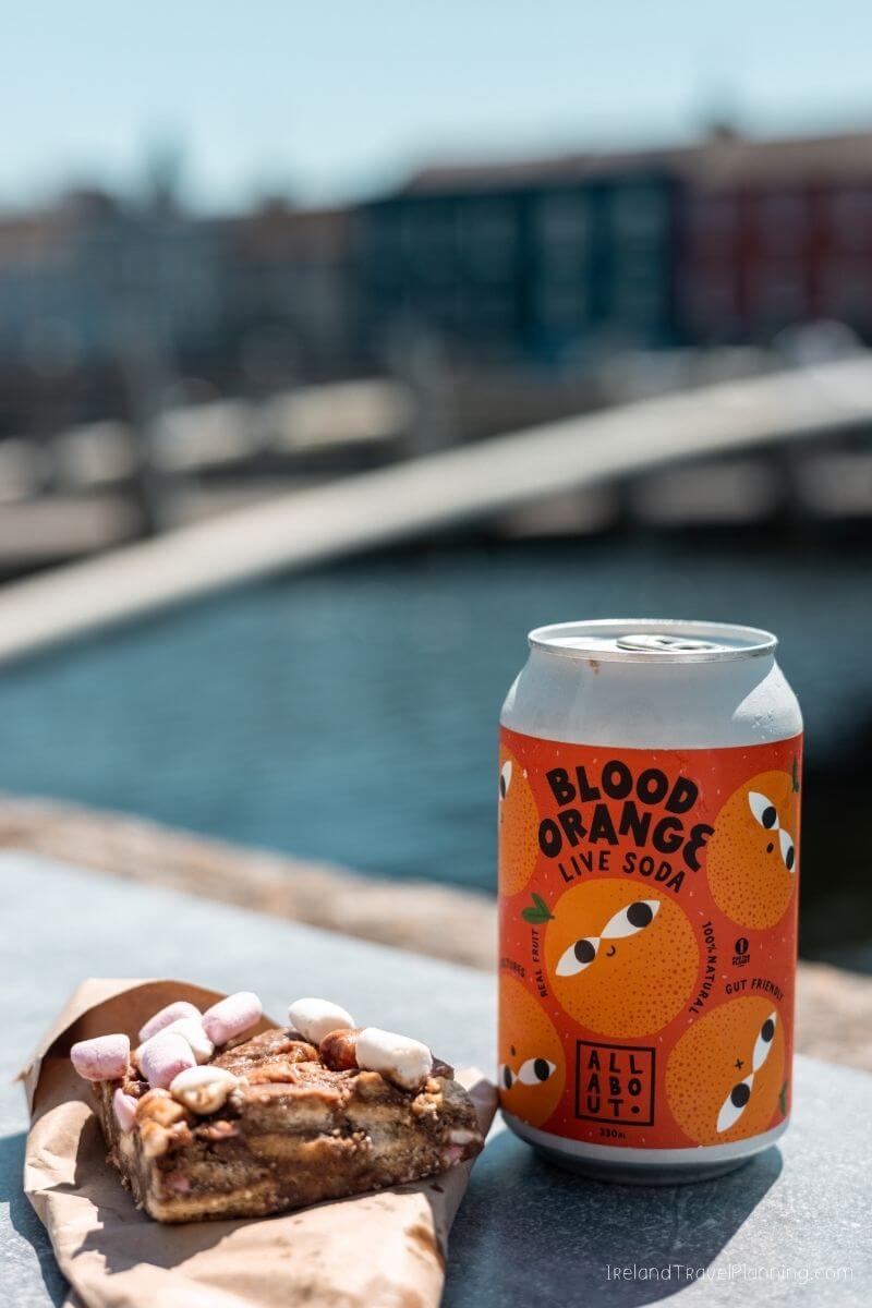 Blood Orange soda can with dessert, both on a table by the river in Cork City