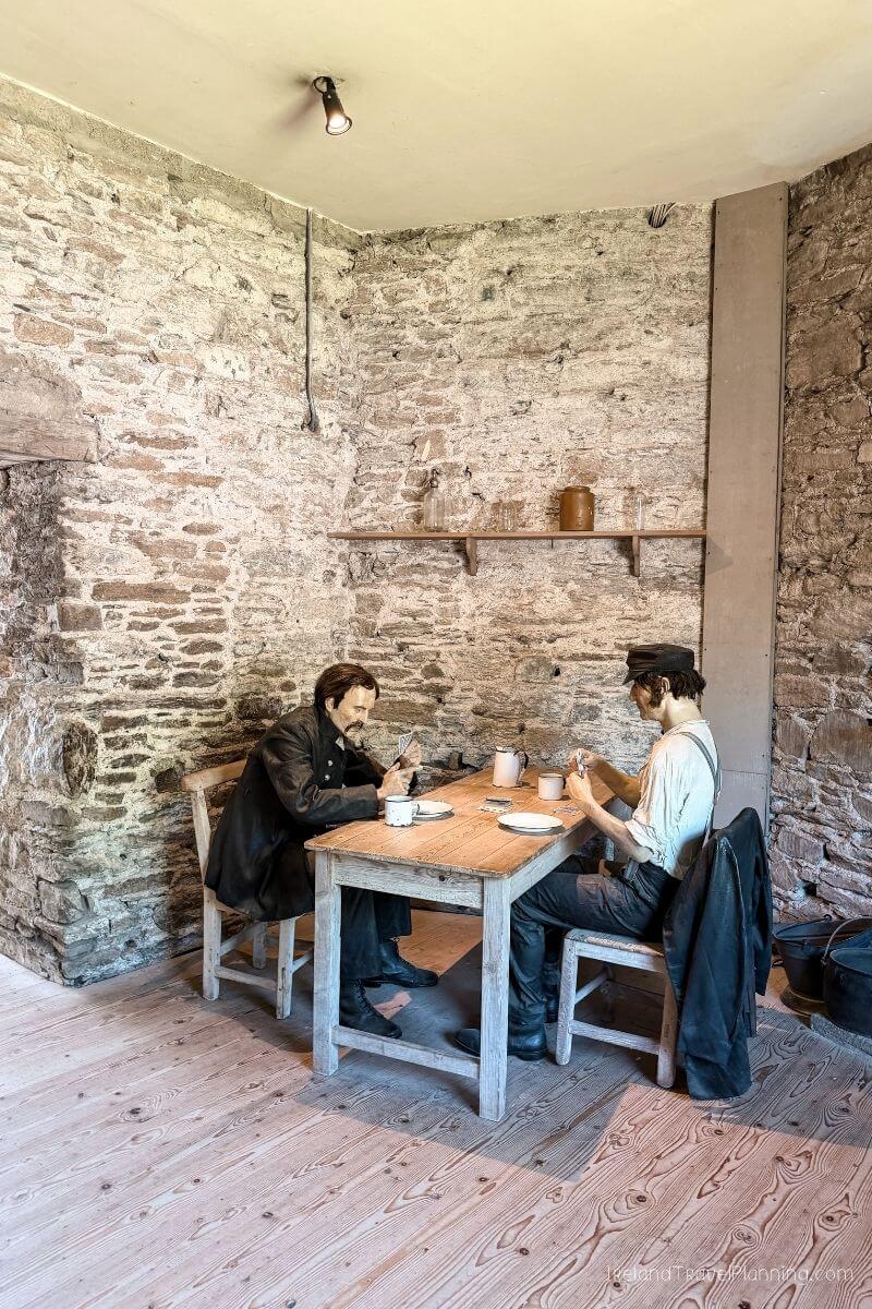 Two men seated in chairs around a table in a stone room in Cork City