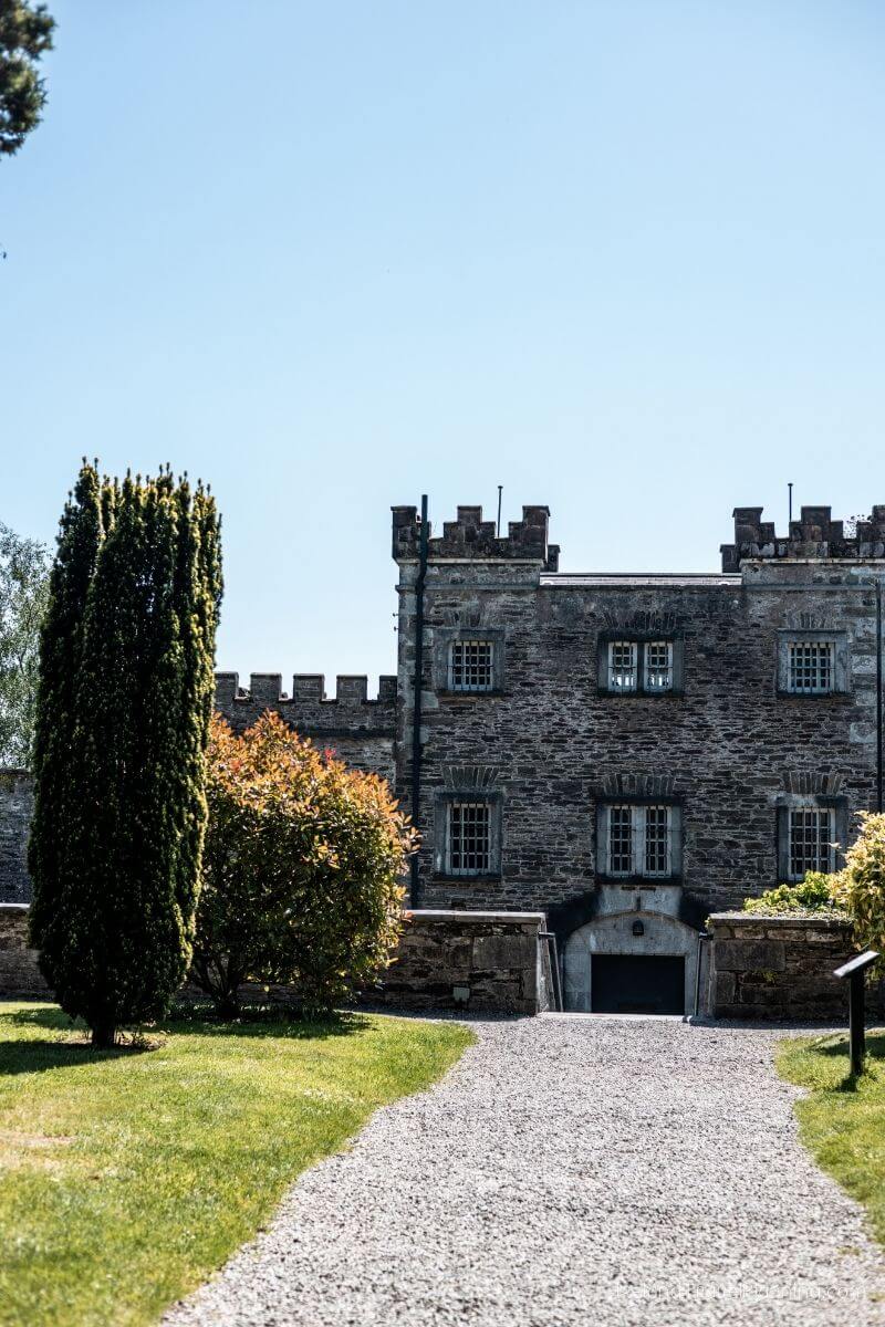Old stone castle with gravel path leading to the entrance, green grass and trees