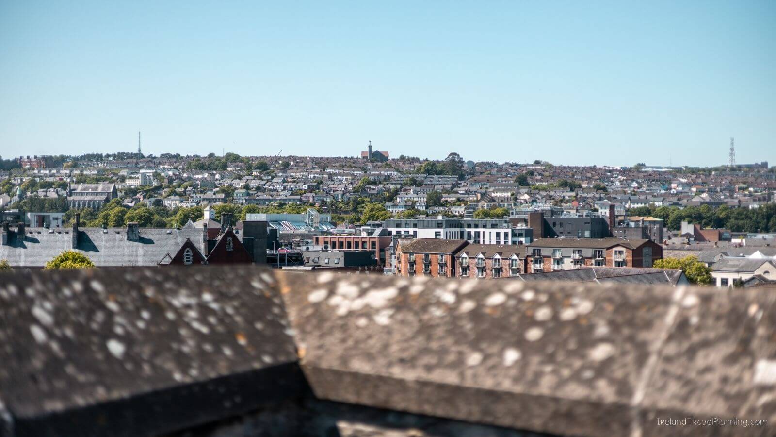 Cityscape view of Cork City with many buildings and trees under a clear sky
